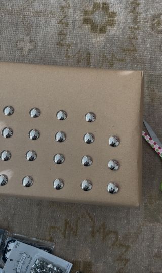 Close up image of a package wrapped in brown wrapping paper halfway done being decorated with silver studs