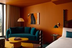 An earthy-hued, modern hotel bedroom features sandy tones and rustic furniture.